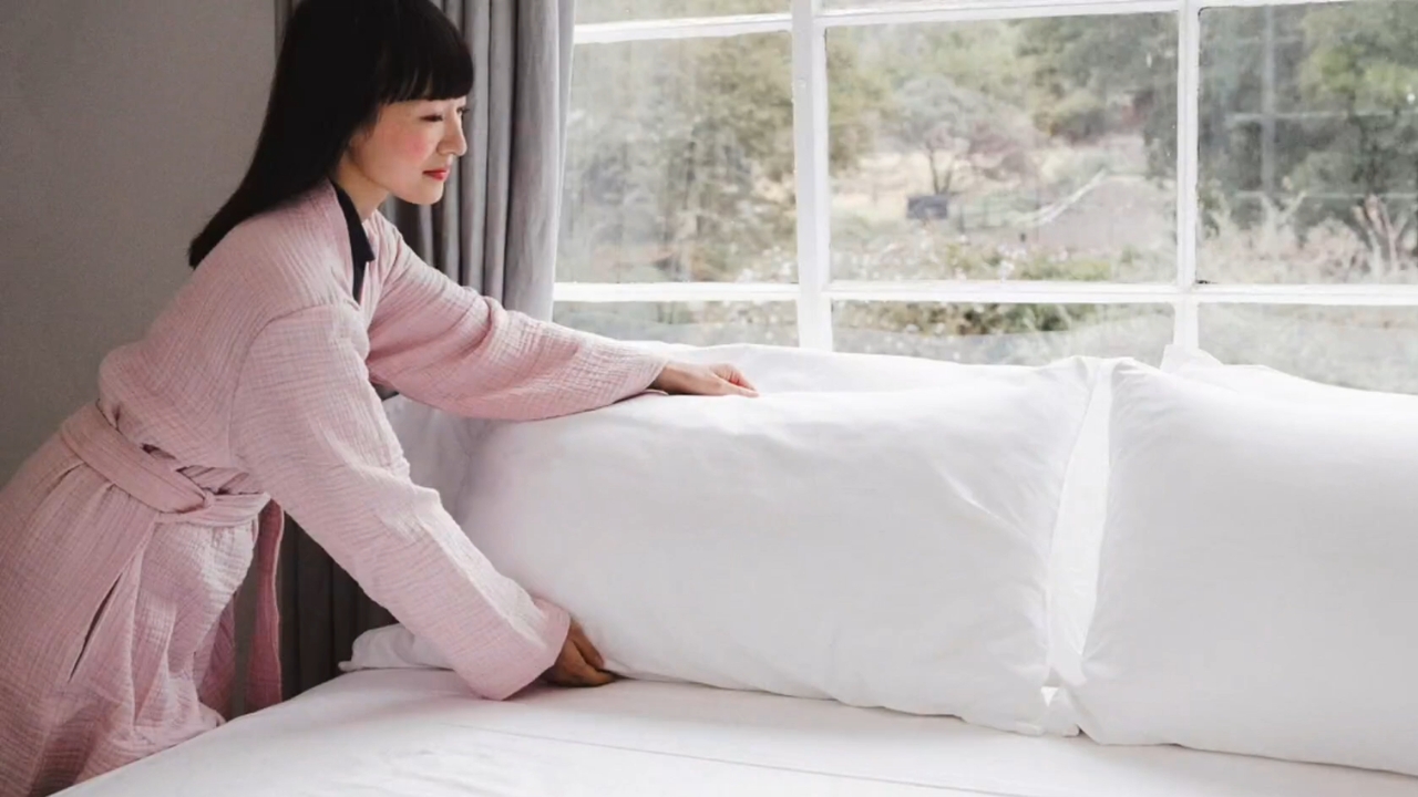 Marie Kondo arranges white pillows on a neatly made bed.