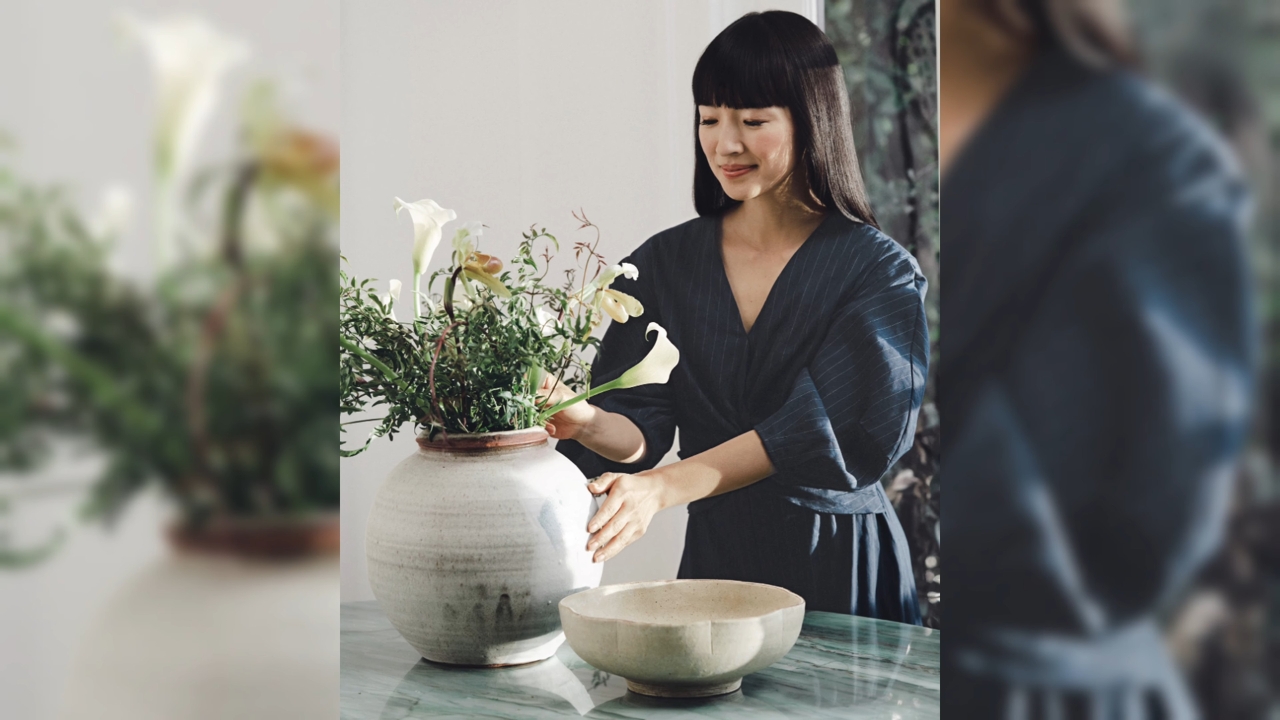 Marie Kondo arranges white flowers in a ceramic vase.